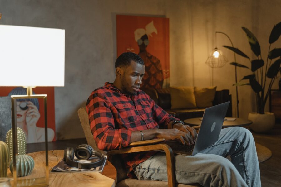 Man in Red and Black Plaid Dress Shirt Sitting on Brown Wooden Armchair Using Laptop