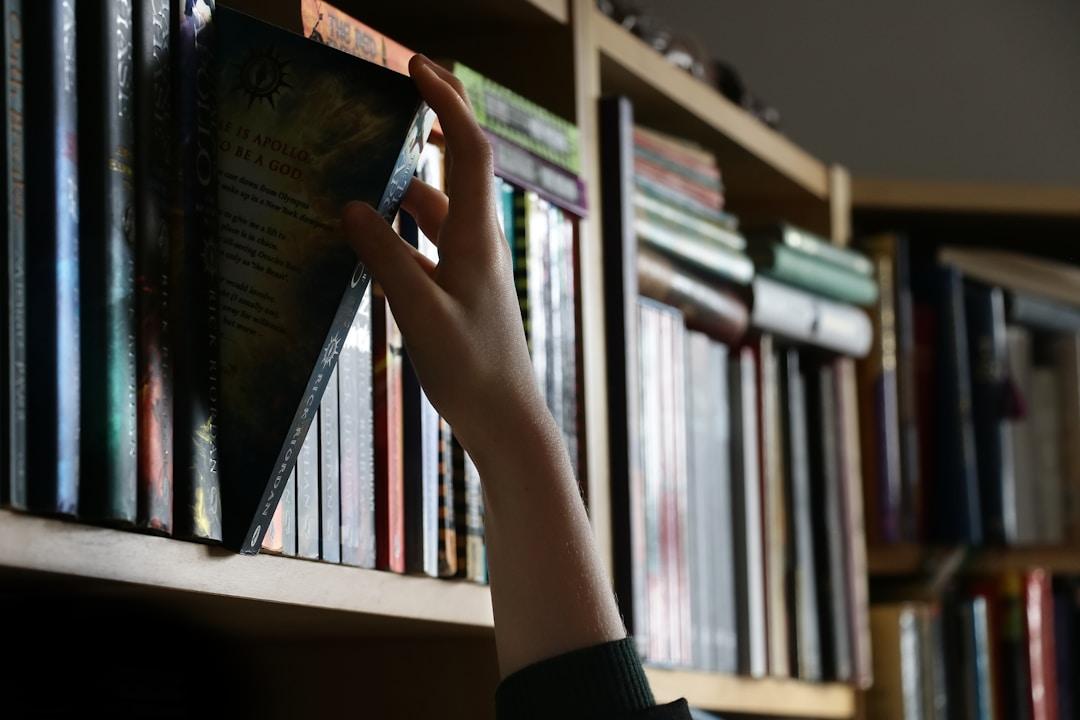 A hand reaches for a book in a library, illustrating how federated search enhances user experience by providing streamlined access to diverse resources.