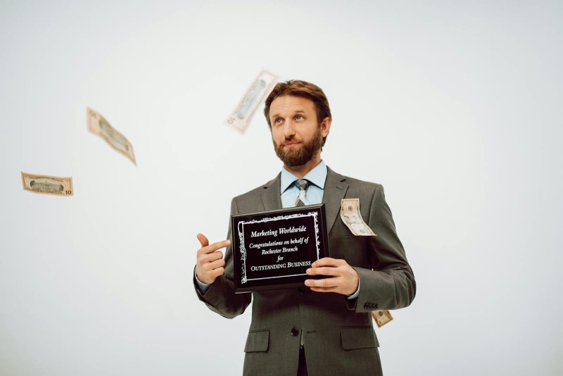Businessman holding an award plaque, surrounded by falling cash, symbolizing success.