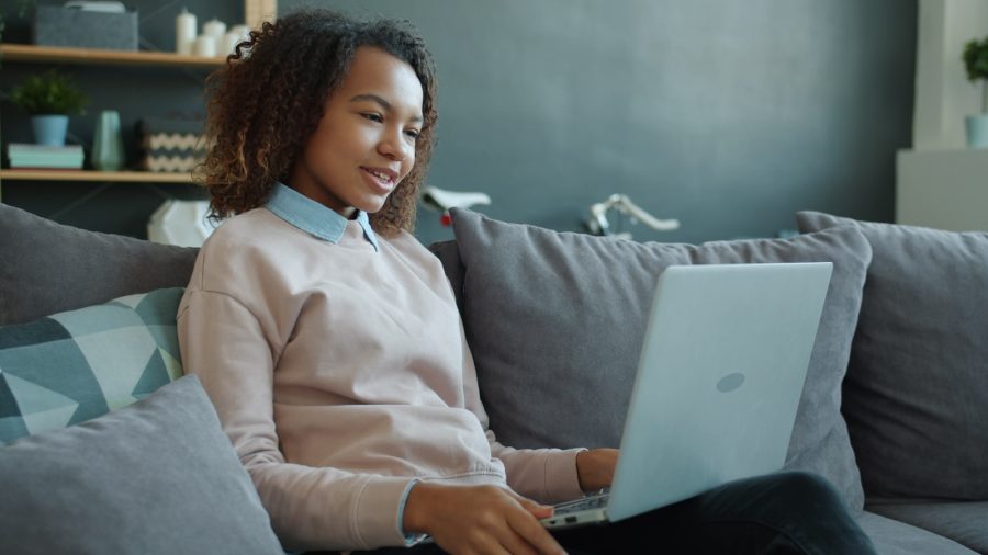 Young woman smiling while using a laptop on the couch.